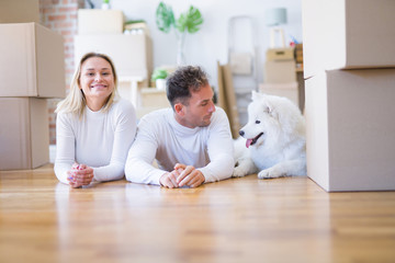 Young beautiful couple with dog lying down on the floor at new home around cardboard boxes