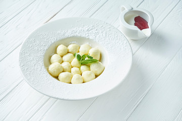 Traditional Ukrainian lazy dumplings. Dumplings with cottage cheese in a white plate on a white wooden background with berry jam. Tasty and sweet breakfast. Vareniki