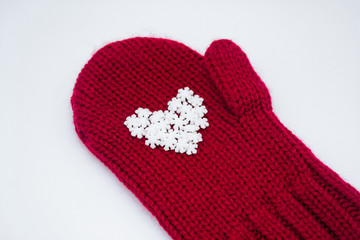 Close up of a knitted red mitten with white snowflakes in the shape of a heart on a white background, isolated. Сoncept of Christmas, winter, love, care and Valentine's day