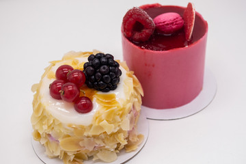 Two cakes on a white background: Bright red with raspberries, berry jelly, macaroon on top and cream cake with almond petals, red currants and blackberries. Concept of holiday, birthday, sweet tooth