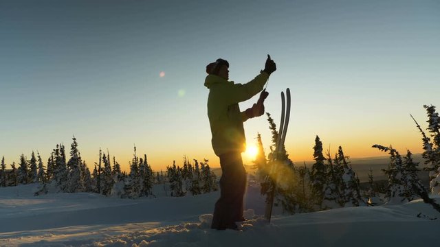 skilled skier holds smartphone in hand and photos sunset