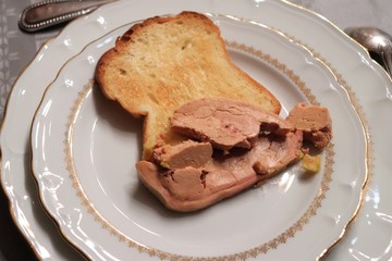 Morceau de foie gras accompagné d'une tranche de pain de mie grillé dans une assiette blanche