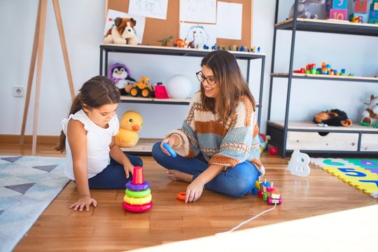 Beautiful teacher and toddler building pyramid using hoops around lots of toys at kindergarten