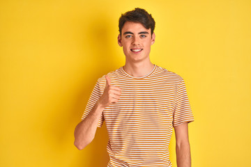 Teenager boy wearing yellow t-shirt over isolated background doing happy thumbs up gesture with hand. Approving expression looking at the camera showing success.