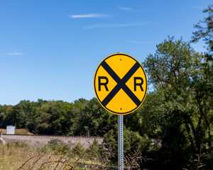 Yellow railroad crossing warning sign on rural road with trees and train tracks in background