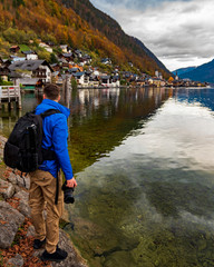 Male photographer standing next to Hallstatt village on Hallstatter lake in Austrian Alps / Evening light during autumn