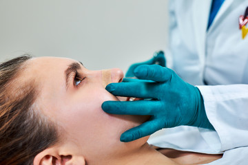 Lady with plaster on nose, doctor examining patients face after plastic surgery