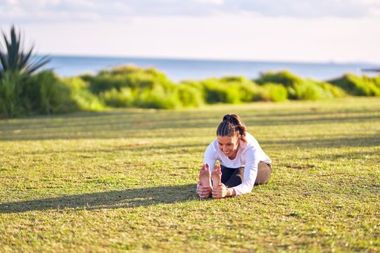 Young beautiful sportwoman smiling happy practicing yoga. Coach sitting with smile on face teaching seated forward fold pose at park