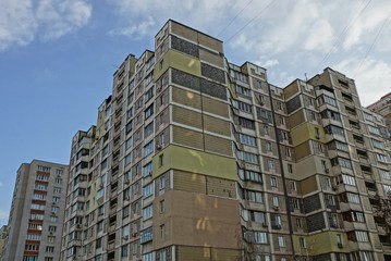 part of a large brown panel house with windows and balconies against the sky and clouds on a sunny day