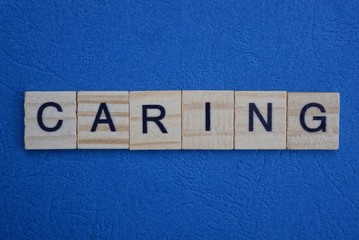 gray word caring from small wooden letters on a blue table