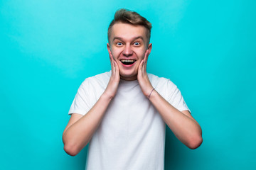 Teen young man looking unpleasantly shocked, scared or worried, mouth wide open and covering both ears with hands against green background