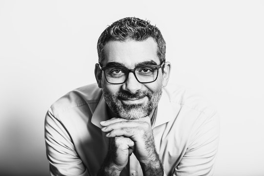 Black and white portrait of handsome man wearing blue shirt and glasses, leaning on hands, posing on white background