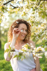 Young attractive girl walks in spring green park enjoying flowering nature. Healthy smiling girl spinning on the spring lawn. Allergy without