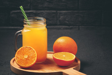 Obraz na płótnie Canvas Homemade freshly squeezed orange juice in a mason jar and oranges on wooden dish on a black background, copyspace