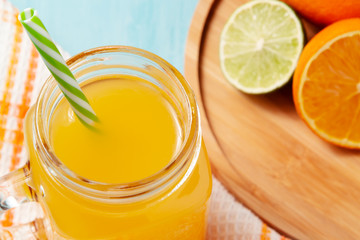 Homemade freshly squeezed orange juice in a mason jar, oranges and lime on wooden dish closeup