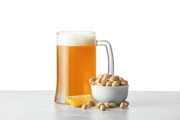 Mug of tasty beer with pistachio nuts on white background