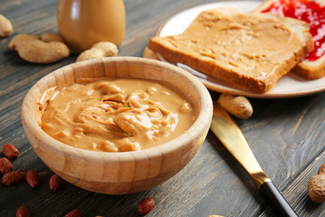 Tasty peanut butter in bowl on wooden table