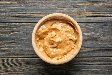 Tasty peanut butter in bowl on wooden table