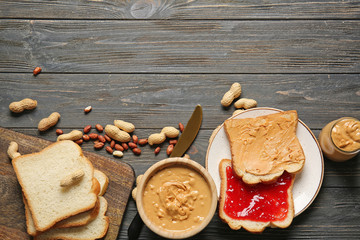 Tasty peanut butter in bowl and fresh bread with jam on wooden table