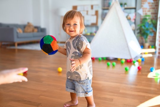Adorable toddler playing with balls around lots of toys at kindergarten