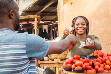 black girl selling tomatoes in a local african market to a male customer smiling and feeling happy...