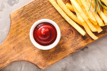 Tasty french fries and tomato sauce on wooden board