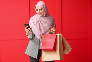 Beautiful Arab woman with shopping bags and mobile phone on color background