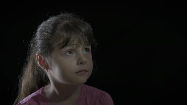 Watch to the fear. Portrait of a scared child. Portrait of a frightened little girl on a dark background.
