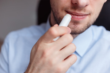 Man applying hygienic lipstick on lips to revive chapped lips and avoid dry, closeup