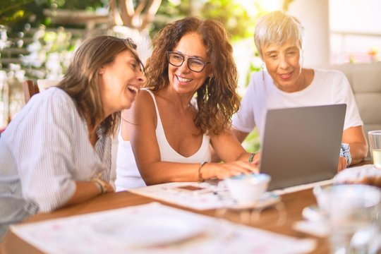 Meeting Of Middle Age Women Having Lunch And Drinking Coffee. Mature Friends Smiling Happy Using Laptop At Home On A Sunny Day