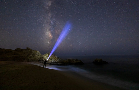 The Milky Way off the coast of Half Moon Bay, Northern California with a man holding a flashlight pointing up into the sky