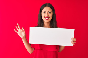 Young beautiful chinese woman holding banner standing over isolated red background doing ok sign with fingers, excellent symbol