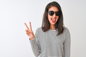 Chinese woman wearing striped t-shirt and sunglasses standing over isolated white background smiling with happy face winking at the camera doing victory sign. Number two.