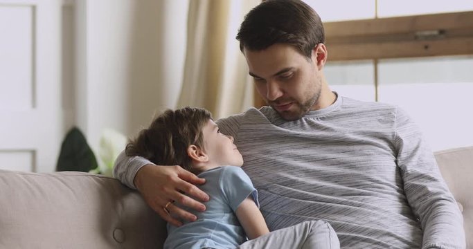 Caring dad embracing preschool son having trust conversation on sofa