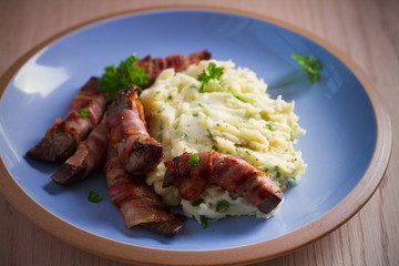 Beef liver wrapped in bacon with mash potato on blue table. horizontal image