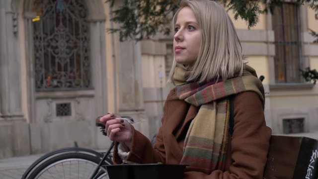 woman eating a satad on city beanch