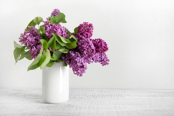 Bouquet of purple lilac flowers in white vase. Space for text.