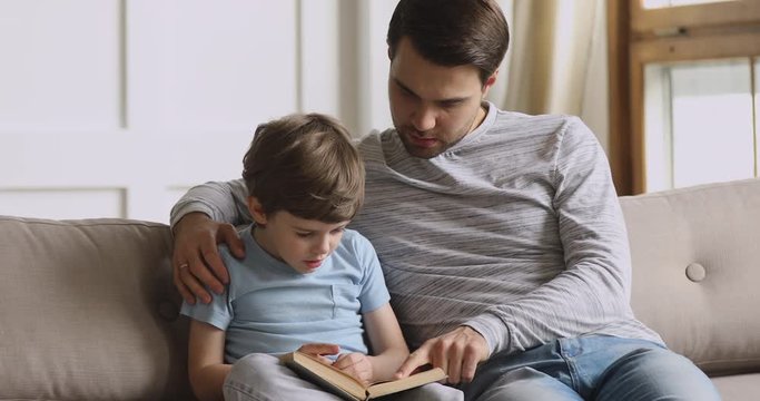 Caring dad teach focused preschool child son reading book