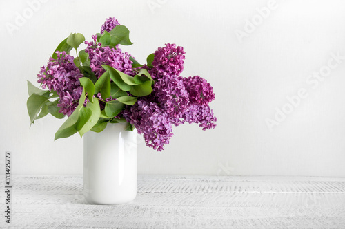 Bouquet of purple lilac flowers in white vase. Space for text.
