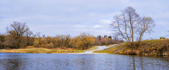Landscape. Trees, dry grass and a country road along the banks of a small river in late autumn.