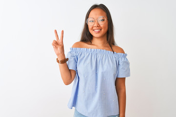 Fototapeta premium Young chinese woman wearing blue t-shirt and glasses over isolated white background showing and pointing up with fingers number two while smiling confident and happy.