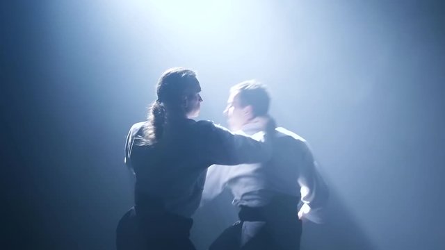 Fight between two aikido fighters in dark studio with smoke and lighting. Slow motion. Close up.