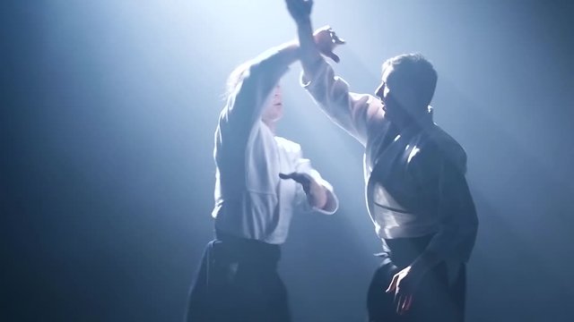 Fight between two aikido fighters in dark studio with smoke and lighting. Slow motion. Close up.