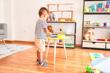 Beautiful toddler boy playing meals with plastic plates, fruits and vegetables at kindergarten