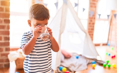 Beautiful toddler boy drinking glass of water at kindergarten