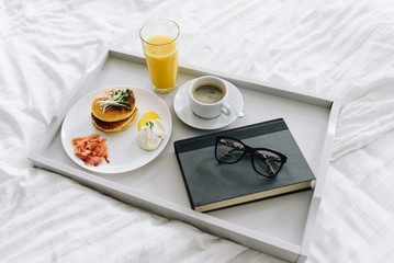Nutritious and tasty breakfast in bed on tray with coffee, orange juice, glasses and book