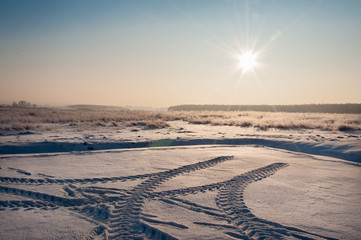 Winter landscape. The rising sun on the background of the field and traces of special equipment.