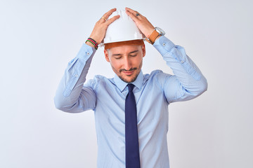 Young business man wearing contractor safety helmet over isolated background suffering from headache desperate and stressed because pain and migraine. Hands on head.