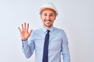 Young business man wearing contractor safety helmet over isolated background showing and pointing up with fingers number five while smiling confident and happy.