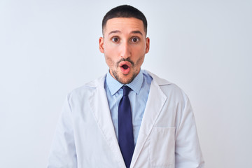 Young doctor man wearing white coat over isolated background afraid and shocked with surprise expression, fear and excited face.